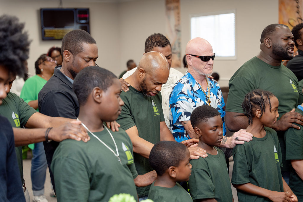 Adults and children of the congregation praying together with hands on one another's shoulders