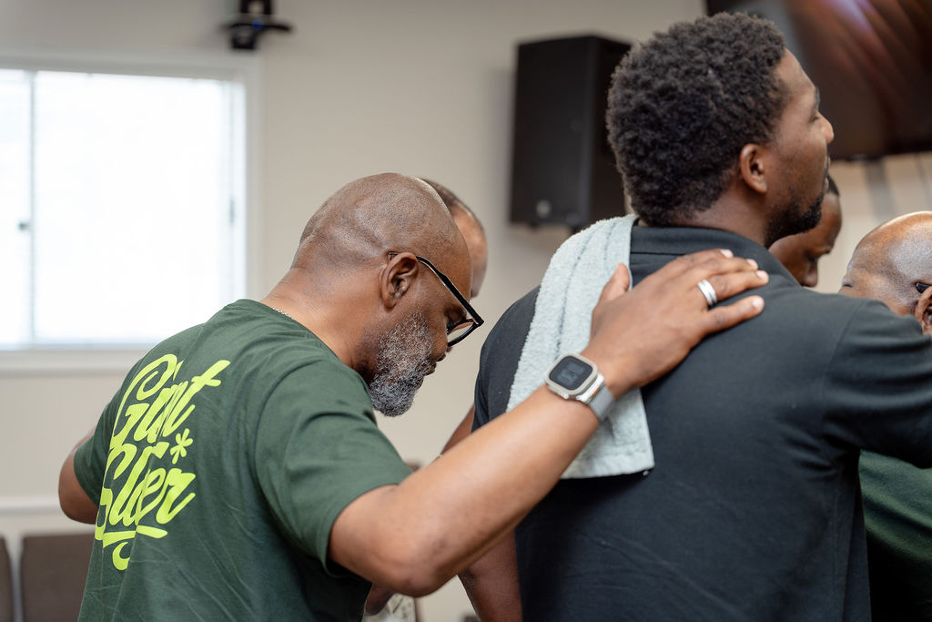 Men praying together with hands on one another's shoulders